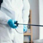 Man wearing protective gear spraying pesticides inside a building