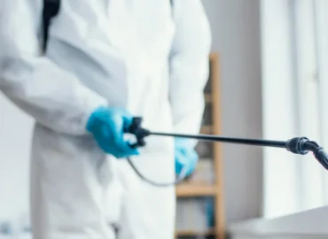 Man wearing protective gear spraying pesticides inside a building