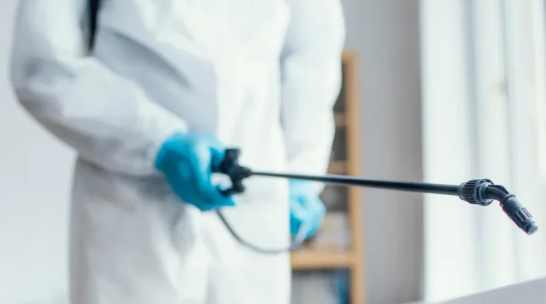 Man wearing protective gear spraying pesticides inside a building